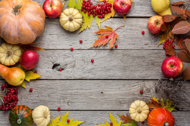 Autumn background with yellow maple leaves, red apples and pumpkins. Frame of fall harvest on aged wood.