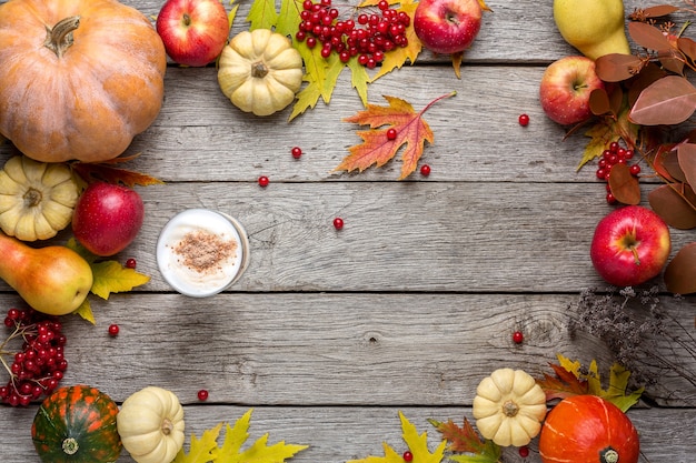 Autumn background with yellow maple leaves, red apples,pumpkins and spicy latte. Frame of fall harvest on aged wood.