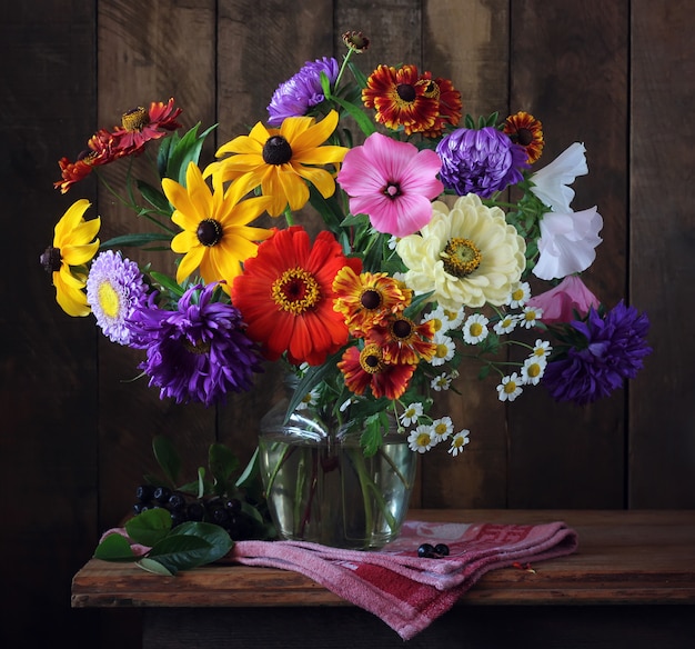 Autumn bouquet of cultivated flowers  in a vase and a branch of black chokeberry on the table.