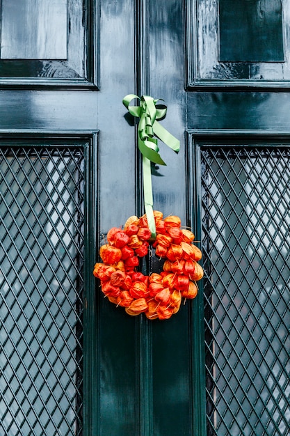 Autumn bouquet of dried orange flowers on a green entrance door to the house. Vertical.