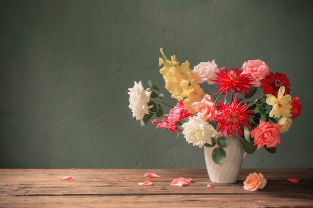 Autumn bouquet with red and yellow flowers in white vase on dark background