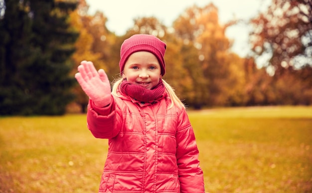 autumn, childhood, gesture, nature and people concept - happy little girl waving hand in park