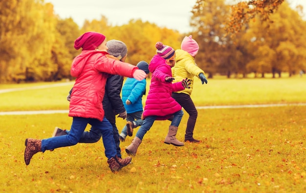 autumn, childhood, leisure and people concept - group of happy little kids playing tag game and running in park outdoors