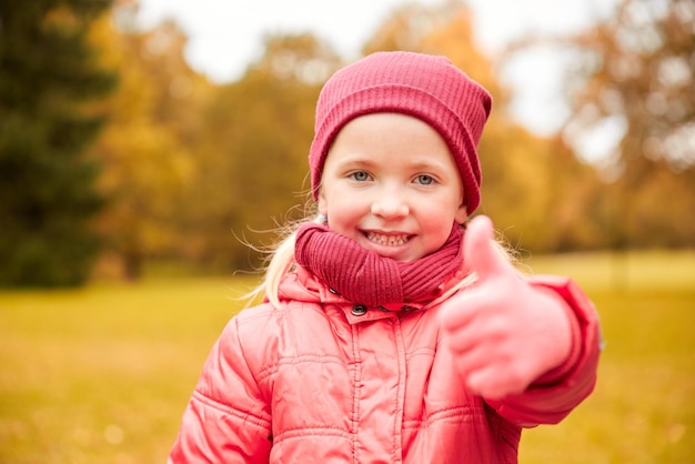 autumn, childhood, nature and people concept - happy little girl showing thumbs up in park