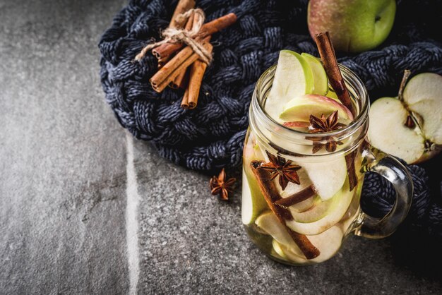 Autumn cocktail. Infused diet detox water with apples and spices - anise, cinnamon. Alcohol cocktail with apple cider. In mason jar on a black stone table. Copy space