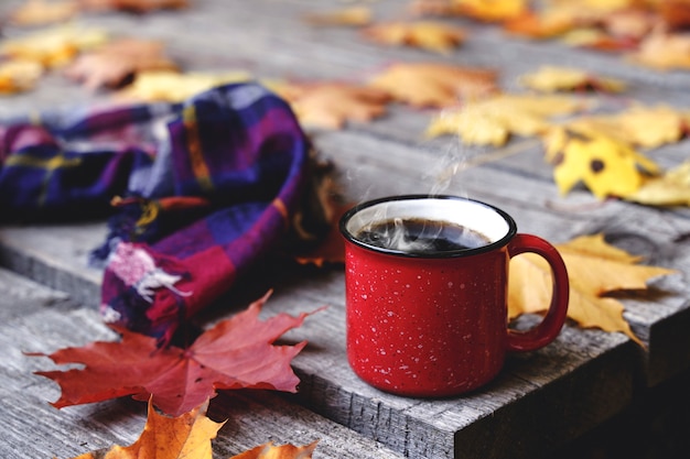 Autumn coffee or tea in a cup on a wooden table against the background of yellow fallen leaves and o...