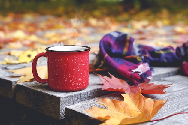 Autumn coffee or tea in a cup on a wooden table against the background of yellow fallen leaves and o...