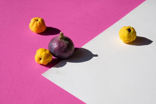 Autumn colors. Purple fig, yellow quince fruits on vibrant fuchsia, magenta and white geometric layered paper. Direct sunlight, long shadows. Simple minimal setup. Bold, brilliant Fall colors, vibes.