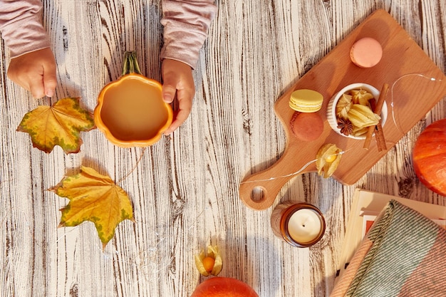 Autumn composition child holding a cup of cocoa and autumn leaves. Macaroons winter cherry pumpkins