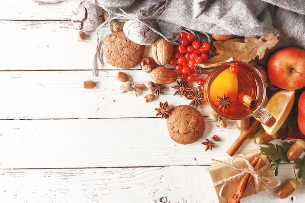 Autumn composition of a cup of warming tea autumn leaves fruits and spices on a white wooden table Top view Copy space