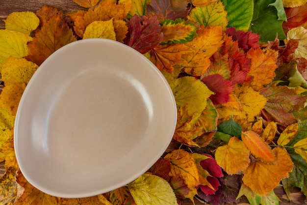 Autumn composition empty plate on colorful autumn leaves Thanksgiving concept fall Flat lay