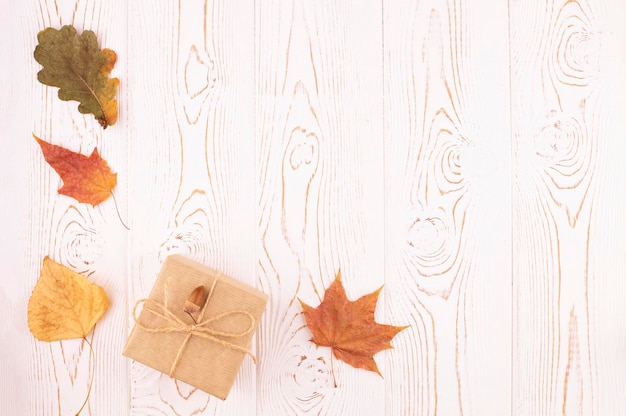 Autumn composition with autumn dry leaves a gift wrapped in kraft paper laid out in a corner on a rustic white wooden background Flat lay copy space