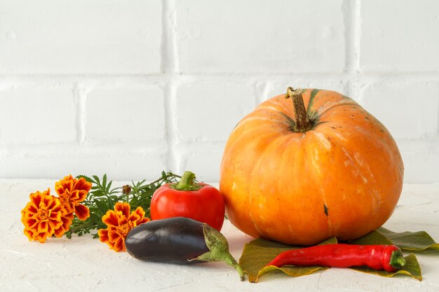 Autumn composition with a big pumpkin and vegetables. Pumpkin and bell pepper, paprica and flowers on a white background. Autumn shopping. Thanksgiving Day.