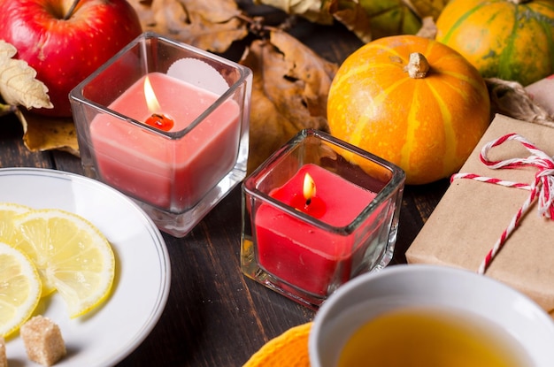 Autumn composition with candles pumpkins and autumn leaves cup of tea on wooden table