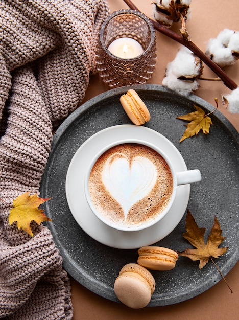 autumn composition with cup of coffee, warm blanket, decorative striped pumpkins, candles and autumn leaves