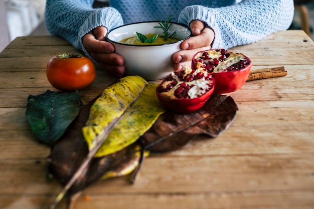 Autumn concept lifestyle at home Close up of people hands holding a cup of tea or coffee Wooden table and decorations fruits Concept of healthy drinking and relax Serene leisure activity indoor