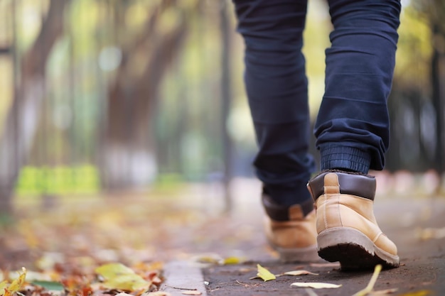 Autumn concept. Pedestrian feet on the road. Autumn leaves on the footpath.