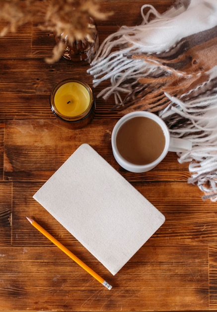 Autumn cozy composition. A cup of coffee, a plaid, a candle, dried flowers on a light background.