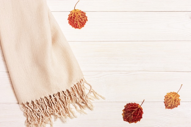 Autumn cozy composition with dried leaves of aspen and pastel beige scarf on wooden background