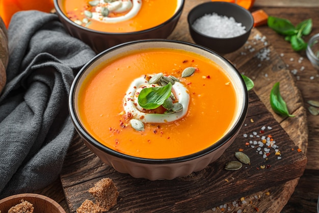 Autumn cream soup with cream and pumpkin seeds on a wooden background. Side view, close-up.