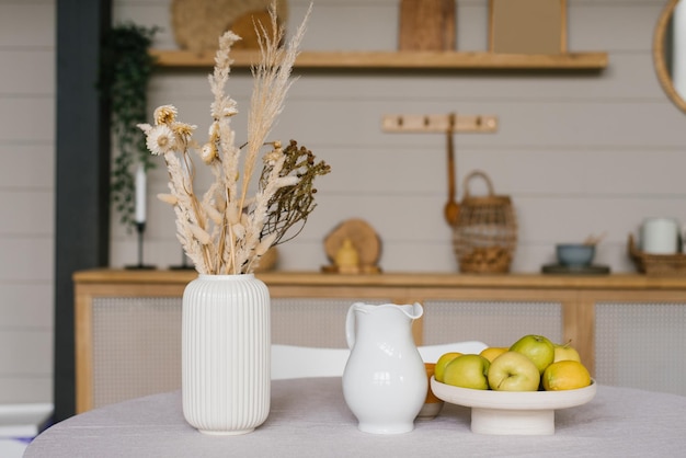 Autumn decor of the dining table Dried flowers in a white ceramic vase a jug of milk and apples on a tray or plate in Scandinavian cuisine