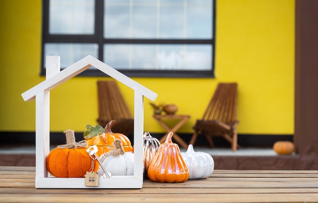 Photo autumn decor on porch of yellow house outside of pumpkin lantern garlands and figure of home and key halloween party autumn mood harvest festival real estate insurance mortgage