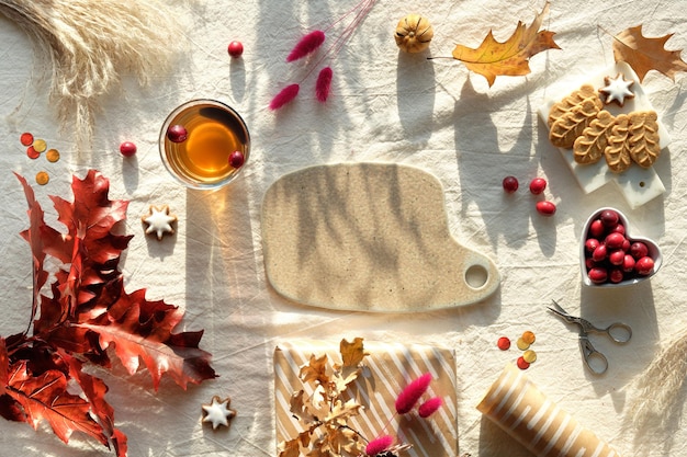 Autumn decorations cranberry cookies tea and dry oak leaves flat lay top view on uncolored textile