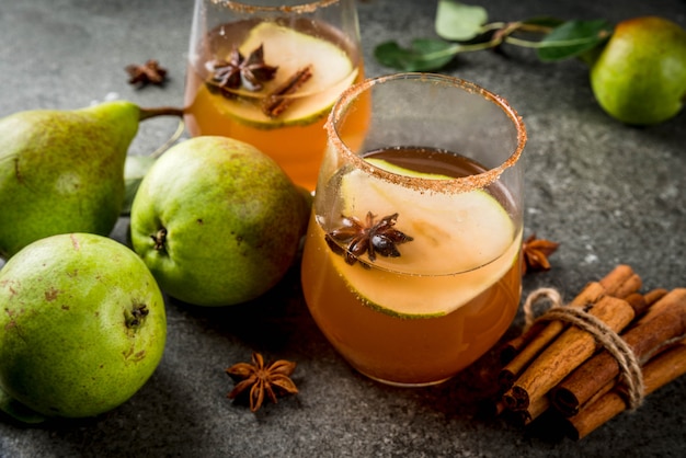 Autumn drinks. Mulled wine. Traditional autumn spicy cocktail with pear, cider and chocolate syrup, with cinnamon, anise, brown sugar. On black stone table. copyspace