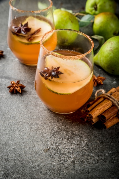 Autumn drinks. Mulled wine. Traditional autumn spicy cocktail with pear, cider and chocolate syrup, with cinnamon, anise, brown sugar. On black stone table. copyspace