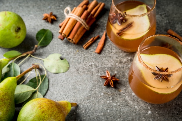 Autumn drinks. Mulled wine. Traditional autumn spicy cocktail with pear, cider and chocolate syrup, with cinnamon, anise, brown sugar. On black stone table. 