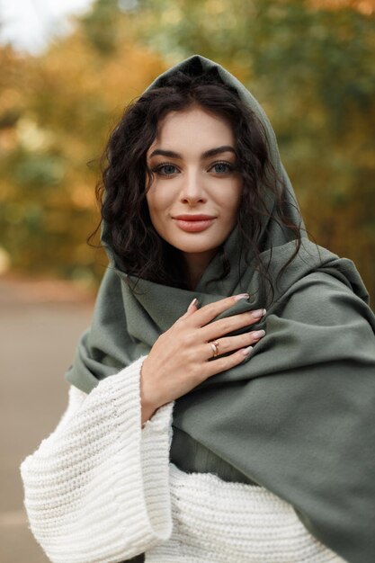 Autumn female portrait of a beautiful young woman with curly hair with a green scarf on her head in a vintage white knitted sweater walks in an fall park