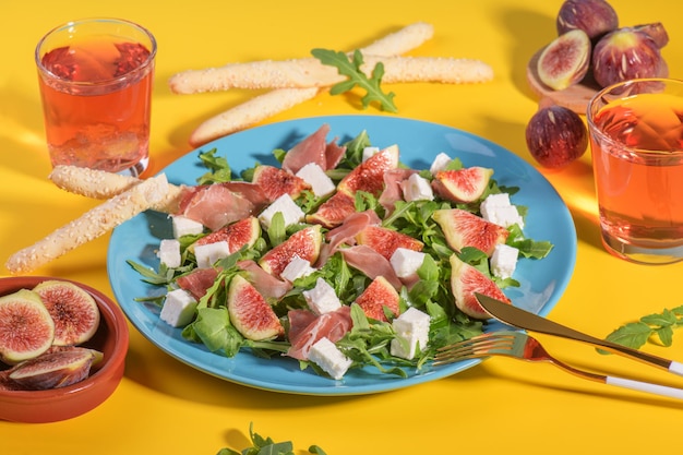 Autumn figs salad with arugula feta raw ham in blue plate on yellow background served with rose wine