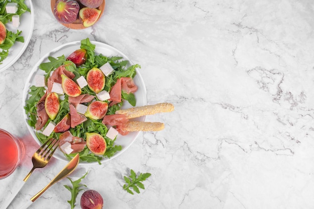 Autumn figs salad with arugula feta raw ham in two white plate on light marlbe background served