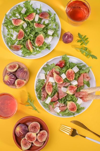 Autumn figs salad with arugula feta raw ham in two white plate on yellow background served with rose