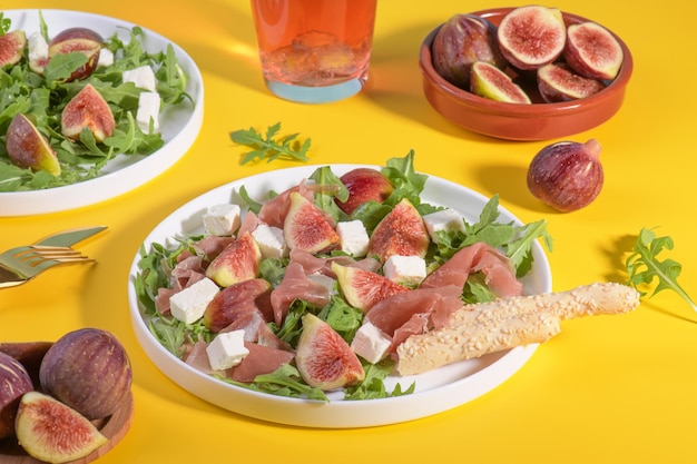 Autumn figs salad with arugula feta raw ham in white plate on yellow background served with rose