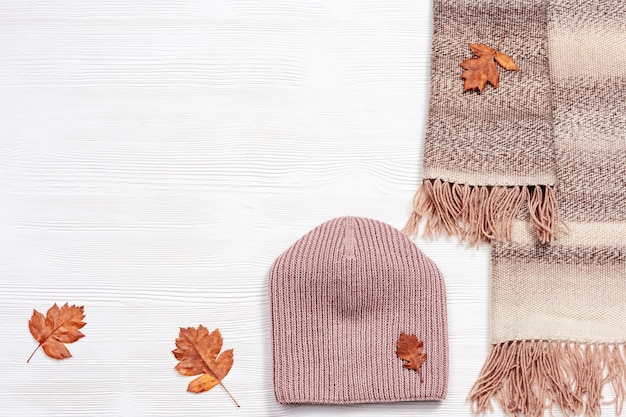 Autumn flat lay with warm woolen scarf and knitted cap Fashion autumn clothes on white wooden desk