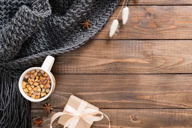 Autumn flatlay composition with cup of herbal tea, wool plaid, gift box and dry flowers on wooden background