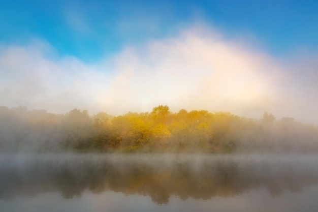 Autumn fog over the river and forest with yellow leaves.