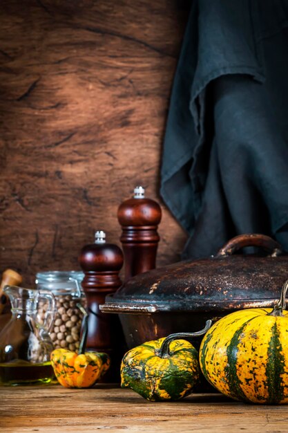 Autumn food cooking background with organic farm broccoli cabbage pumpkins herbs and spices on rustic wood kitchen table with cast iron pan spice grinders cutting board