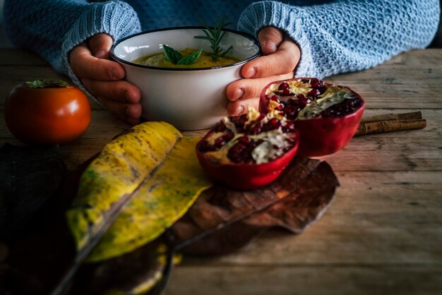 Autumn food and lifestyle concept with close up of woman hands holding warm vegetable soup on a rustic wooden table decorated with yellow leaves People and healthy lifestyle nutrition diet Eating