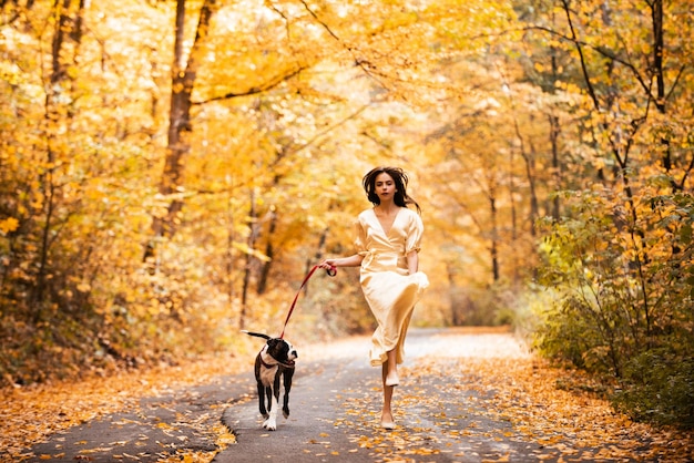 Autumn forest Woman with dog is running over a forest road Cheerful happy young beautiful girl Beaut