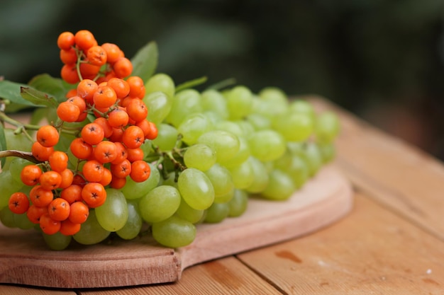 Autumn grapes and rowan berries on a wooden table closeup Ripe green grapes and orange rowanberries on a wooden board on a blurred background