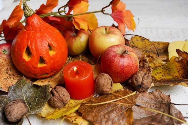 Autumn halloween composition with leaves, apples and pumpkin with face