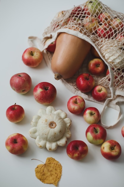 Autumn harvest with sqush pumpkin apples and vegetables in a mesh shopping bag on white background