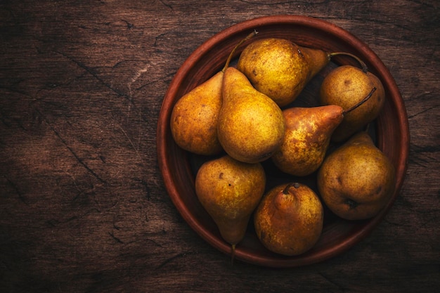 Autumn harvest of yellow pears on clay plate on old rustic wood kitchen table background top view