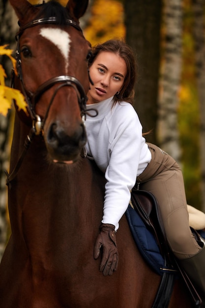 Autumn landscape beautiful brunette girl with long hair posing with a red horse in the forest