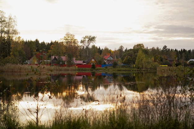 Photo autumn landscape of country houses on pond shore reflecting in water on sunset russia