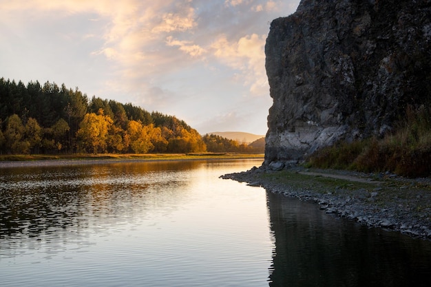 Autumn landscape with a river and a forest A high gloomy rock on one side of the river