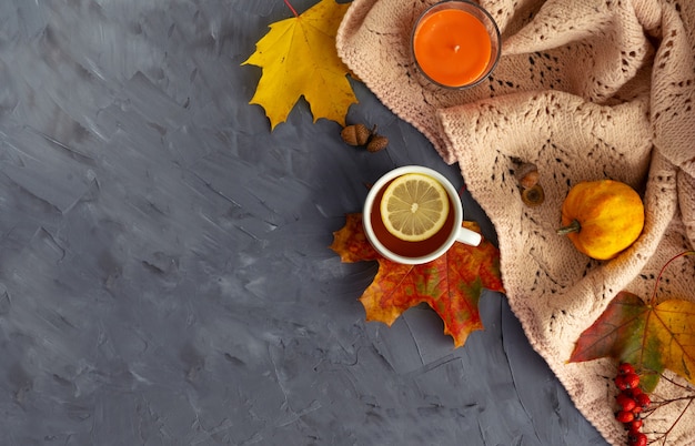 Autumn layout. Fallen bright leaves, aroma candle, cones, pumpkin and cup of hot tea with lemon on a wooden background. Top view