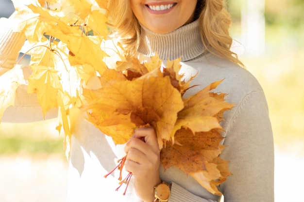 Autumn leaf fall bouquet of bright yellow leaves is held in hands of young woman dressed in light ca